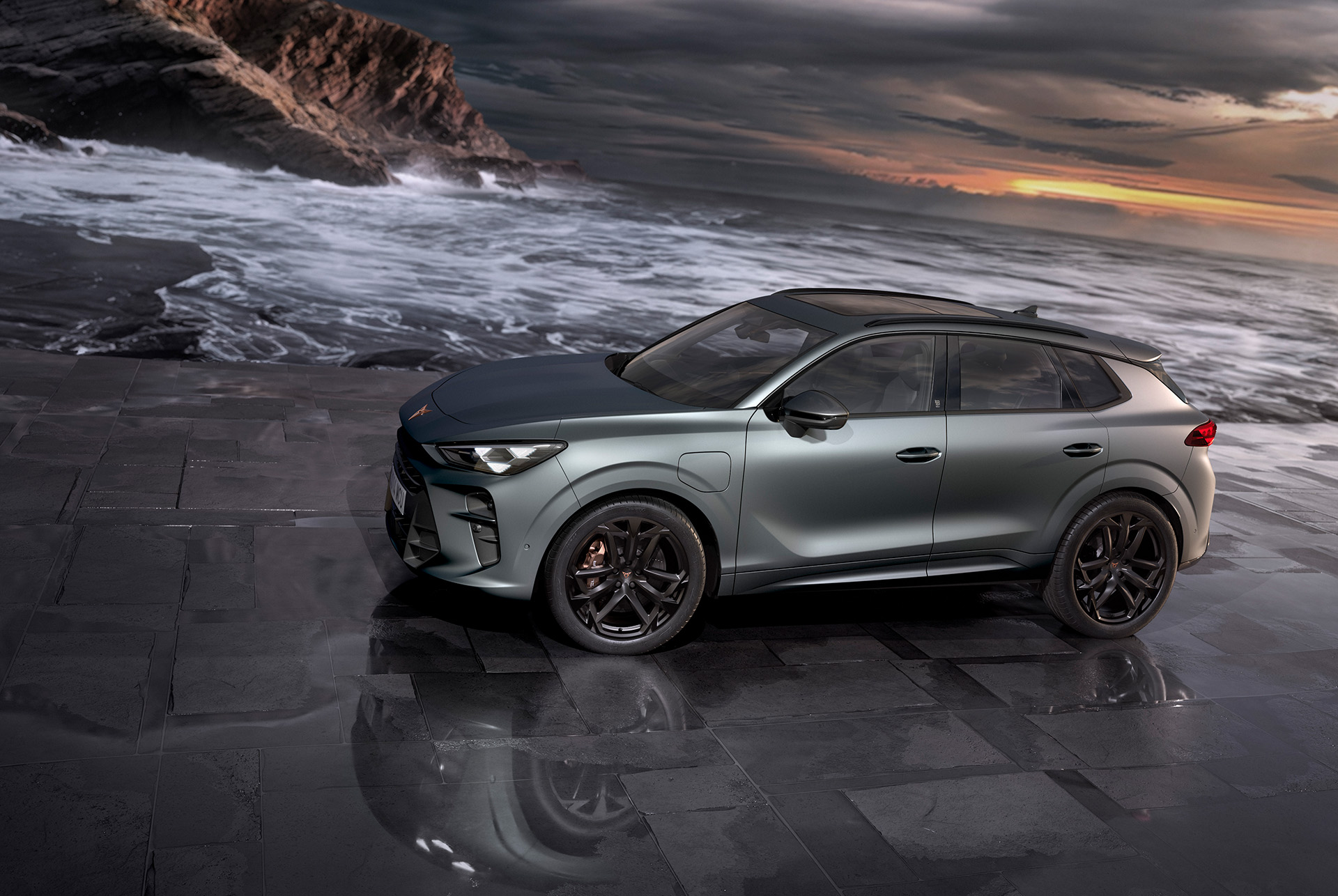 cupra terramar laddhybrid suv, ny 2024-modell, sedd från sidan, med 20-tums america’s cup lättmetallfälgar och akebono-bromsar, enceladus grey matt, på en våt trottoar vid havet i solnedgång. 